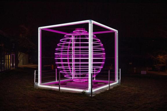 Vue de l'Oeuvre (sphère lumineuse en tubes néon de couleur rose-violette dans un cadre cubique blanc)