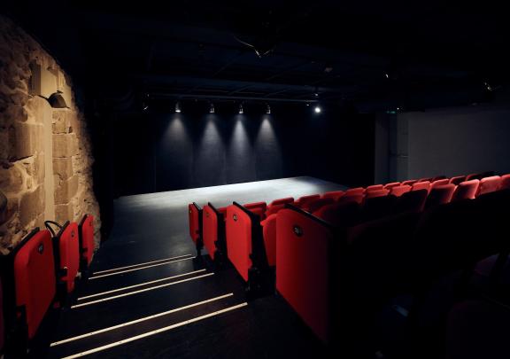 Vue intérieure de la salle du Théâtre du Crève-Coeur: rangées de fauteuils rouges et scène vide