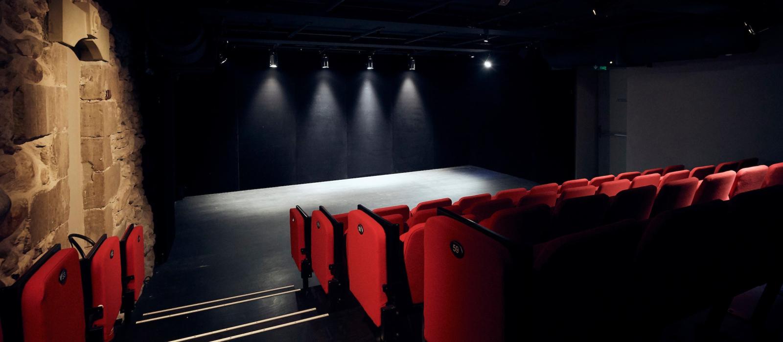 Vue intérieure de la salle du Théâtre du Crève-Coeur: rangées de fauteuils rouges et scène vide